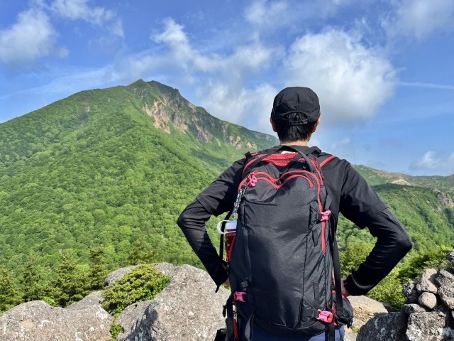 山頂でザックを背負って立つ登山者の後ろ姿